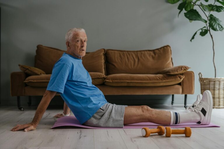 Senior man exercising indoors on a yoga mat with dumbbells. Health and fitness lifestyle.