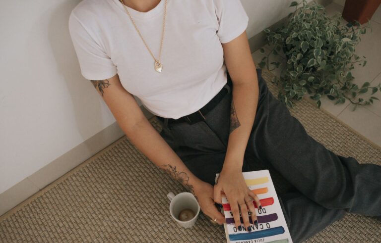 Woman sitting on rug, reading a colorful book with coffee cup nearby.