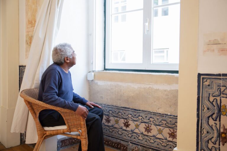 Senior man in a wicker chair gazing out a window, surrounded by traditional Portuguese tiles.