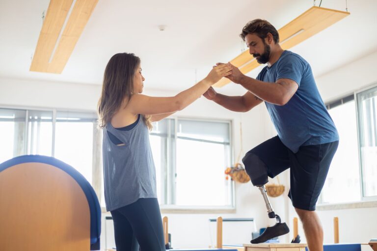 A man with a prosthetic leg exercises with a therapist in a well-lit gym environment.