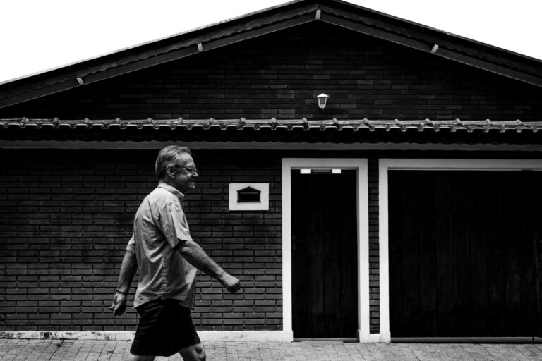 Monochrome image of a man walking in front of a brick building.