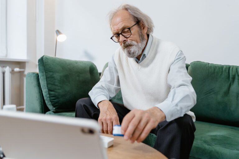 Elderly man with glasses using a tablet for telehealth consultation at home.