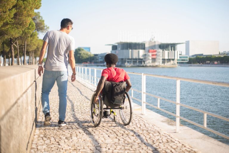 Man and friend in wheelchair strolling along the river in Portugal, showing friendship and accessibility.