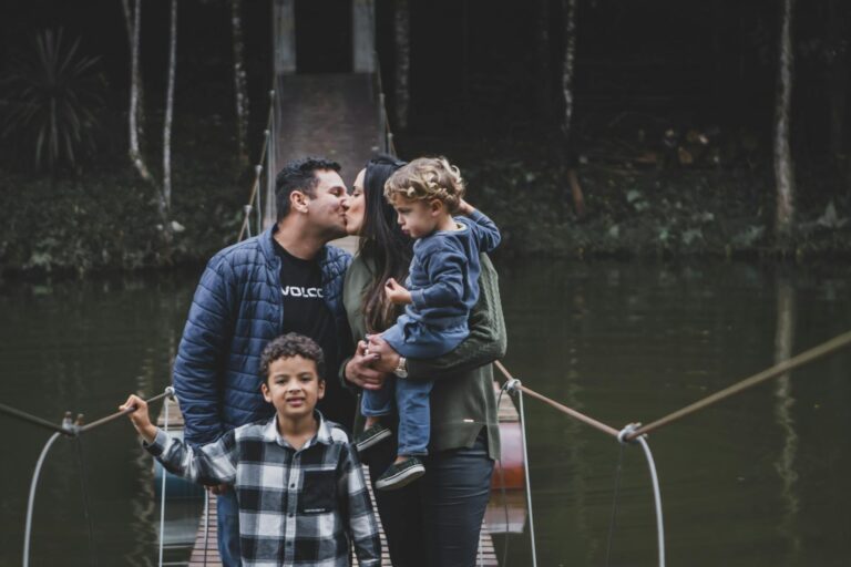 Family kissing on a suspension bridge surrounded by nature.