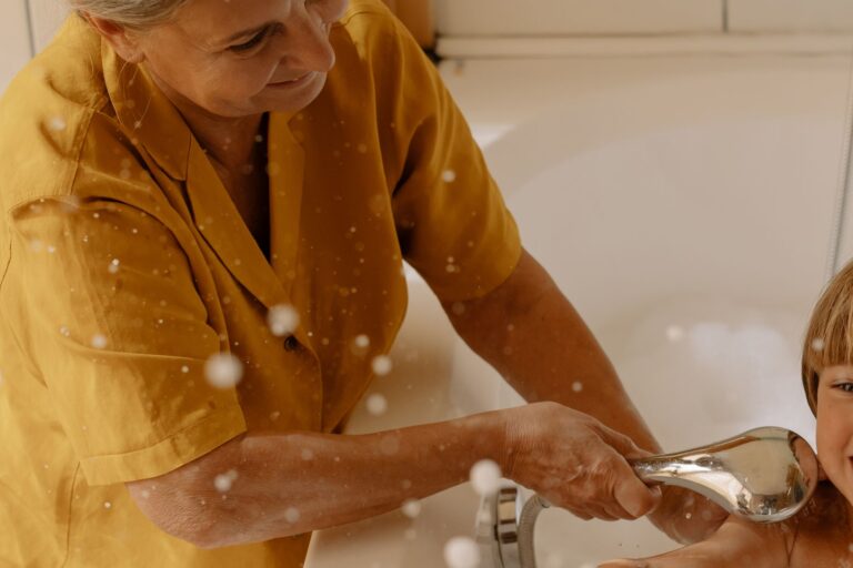 Elderly woman using shower head to bathe her grandson in the bathtub.