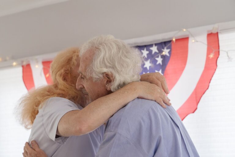 Senior couple embracing with American flag backdrop, celebrating togetherness and freedom.