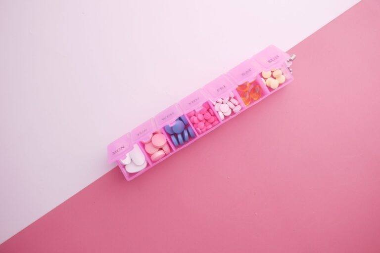 A pink pill organizer with colorful tablets arranged for each day of the week on a vibrant pink background.