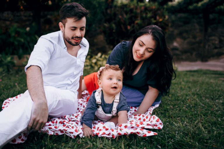 A joyful family enjoying a picnic outdoors during summer. Smiling parents with their baby on a blanket.