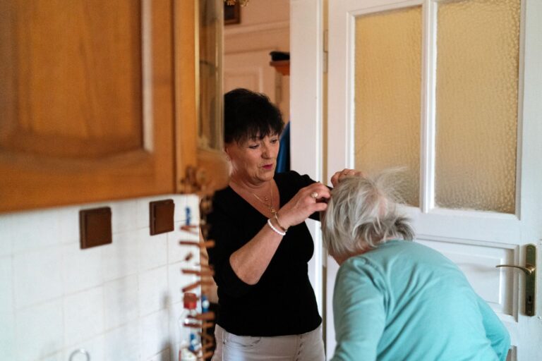 A caregiver helps an elderly woman with grooming in a cozy home environment.