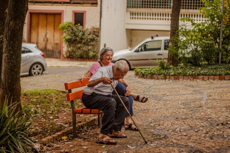 Senior couple enjoying a peaceful moment on a park bench in an urban setting with cars and greenery.