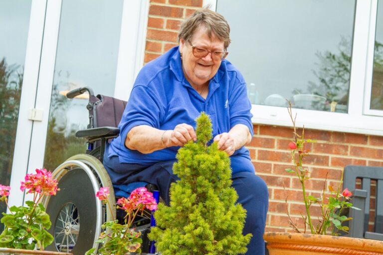 Senior woman in a wheelchair enjoys gardening in her backyard, tending to plants and flowers.