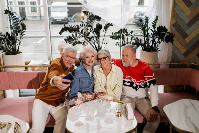 Group of four senior adults taking a selfie together, smiling and enjoying beverages indoors.