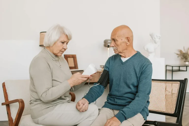 Senior couple measuring blood pressure at home, showcasing care and companionship.