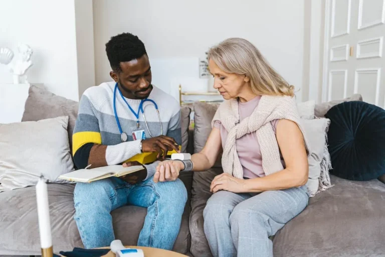 Healthcare professional checking blood pressure of elderly woman in a cozy indoor setting.