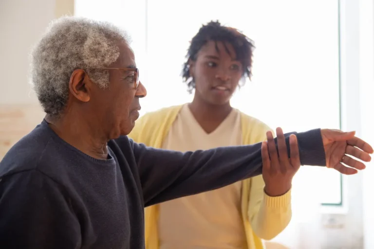 A caregiver helps an elderly man with arm exercises in a warm and caring environment.