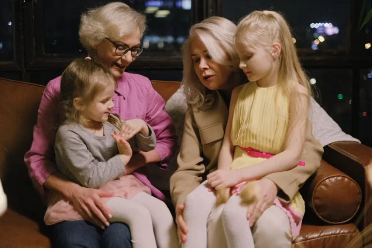 A warm family moment indoors with two grandmothers and two granddaughters sitting together on a sofa.