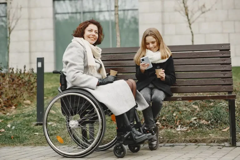 A joyful moment between mother in wheelchair and daughter sharing coffee on a park bench.