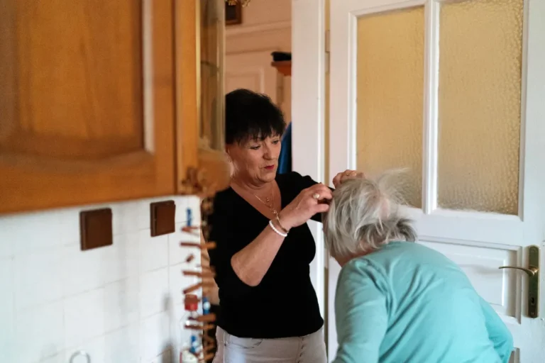 A caregiver helps an elderly woman with grooming in a cozy home environment.